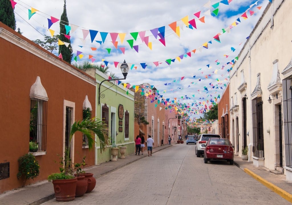 A Mexican street with brightly painted buildings and bright triangular flags hanging on lines between them.