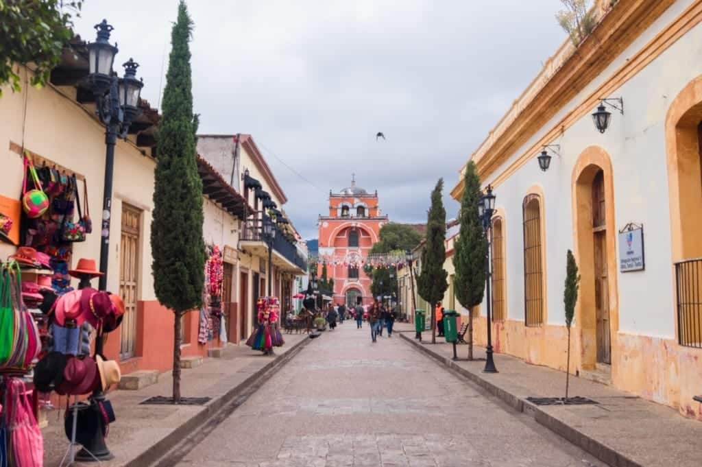 Lots of colorful colonial buildings on a street in San Cristobal, a hat vendor on one side.