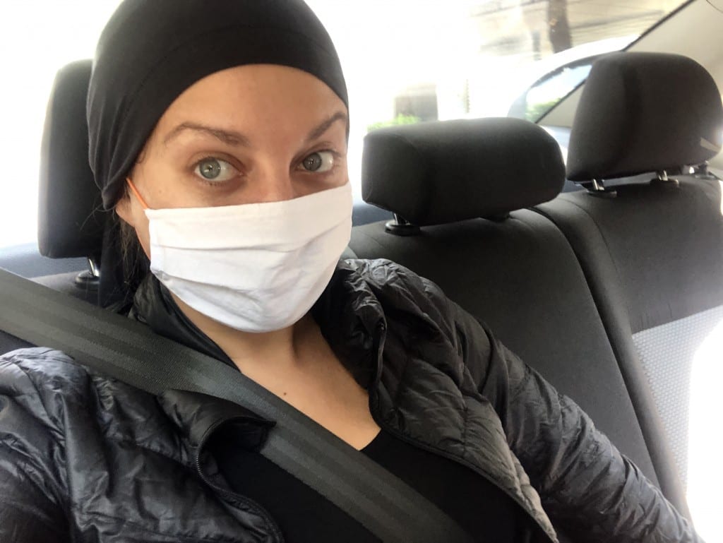 Kate in the back of a car in a mask and black do-rag.