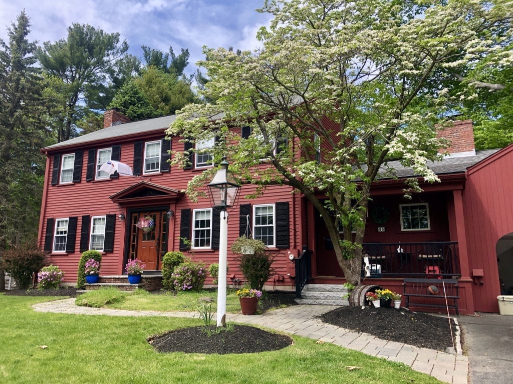 A red colonial-style home with a blossoming white tree in front.