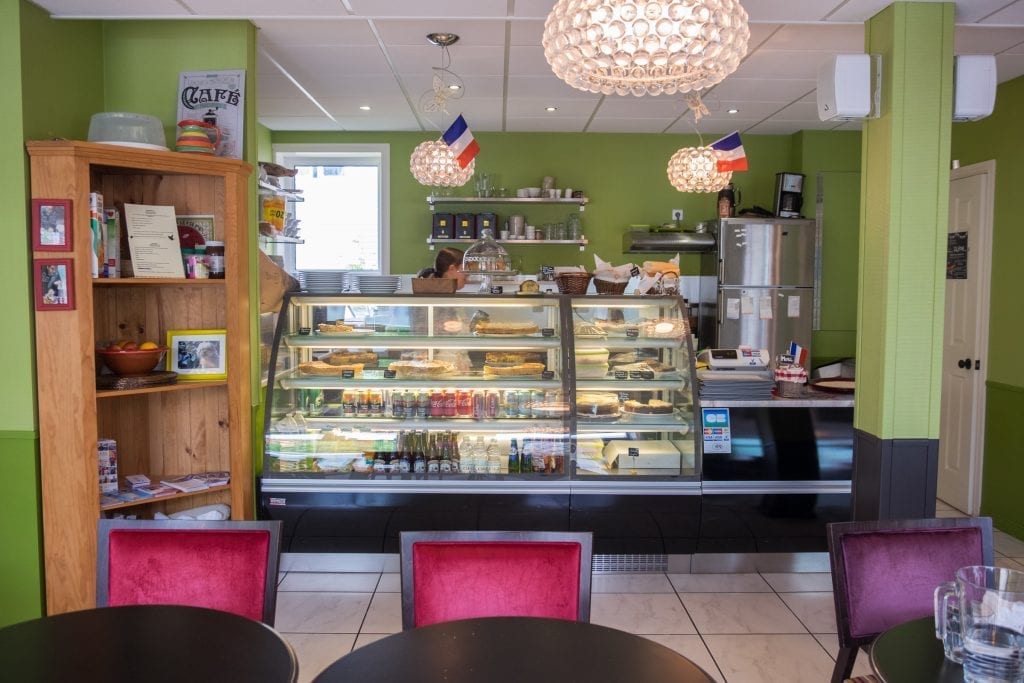 A cafe with pastries and sodas in the glass case and French flags hanging from the ceiling.