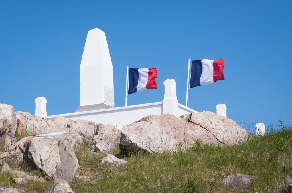 Two French flags waving on top of a white marble monument on top of a rocky hill.