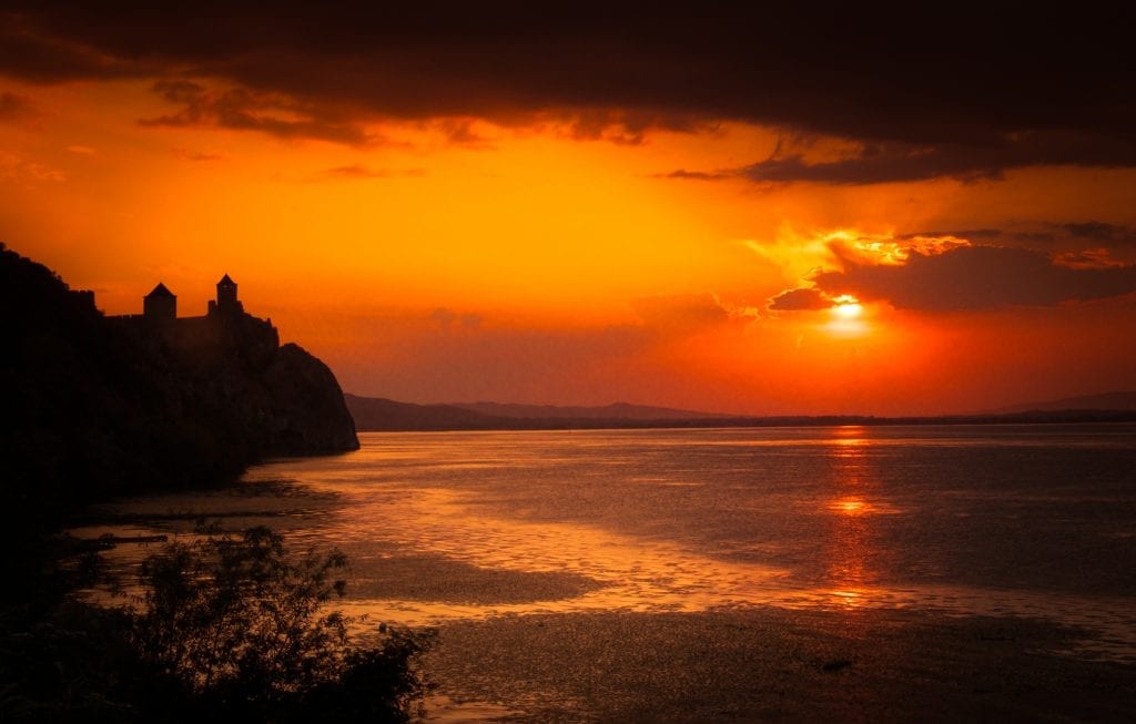 A bright red sunset on the Danube, with the pointy towers of Golubac Fortress silhouetted on the left.