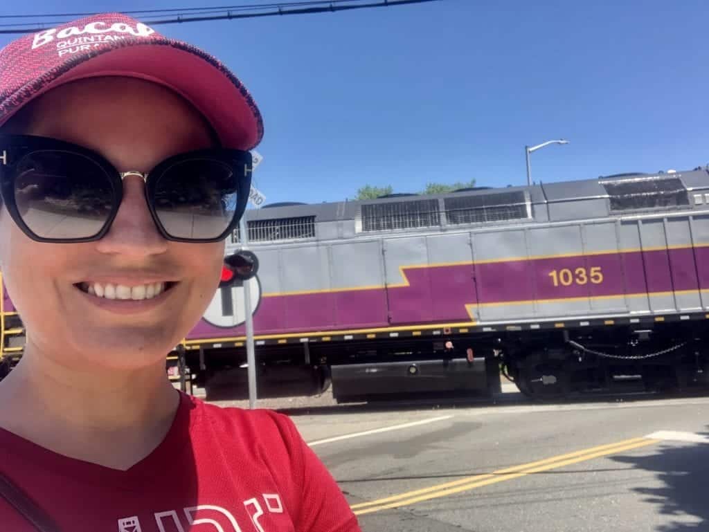 Kate takes a selfie and smiles in front of a purple and gray commuter rail train.