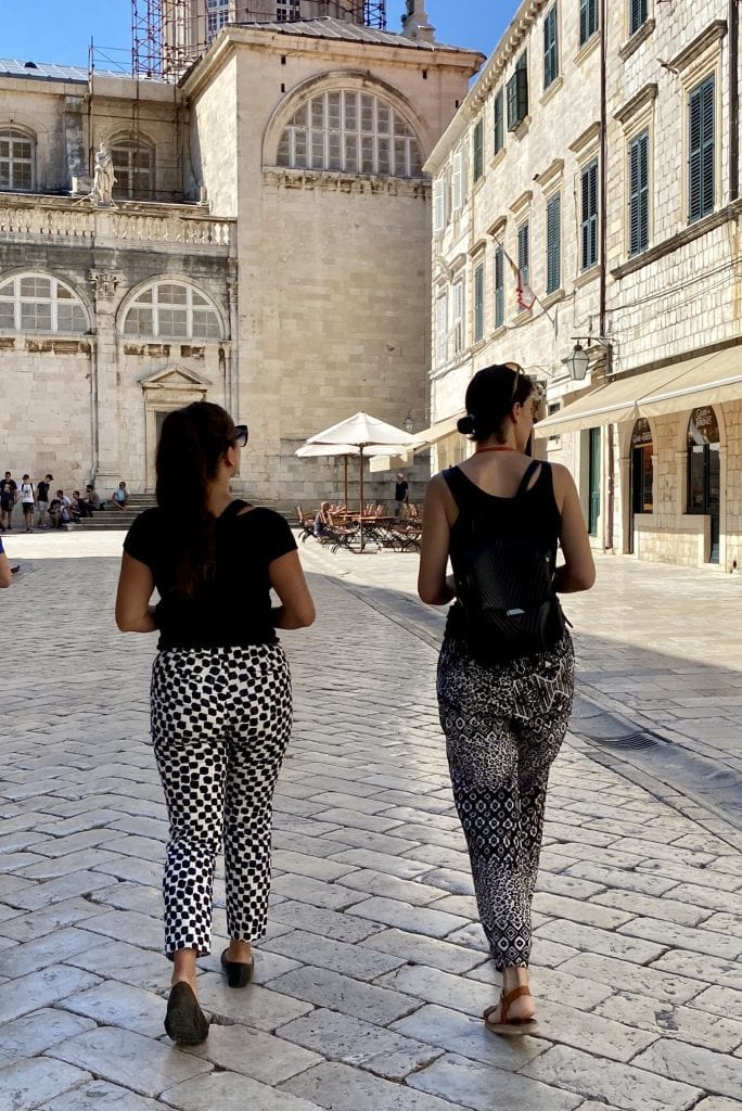 Kate and tour guide Ana walking down an empty street in the old town of Dubrovnik, facing away from the camera. Both wearing black sleeveless tops and black and white printed pants.