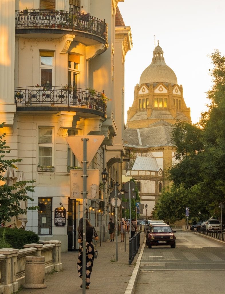 A view of Novi Sad at sunset with the synagogue bathed in golden light in the distance; an apartment building with round balconies in the foreground.