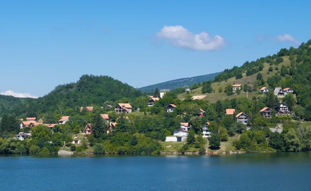 A bright blue lake in Serbia, white houses with orange roofs on the shore.