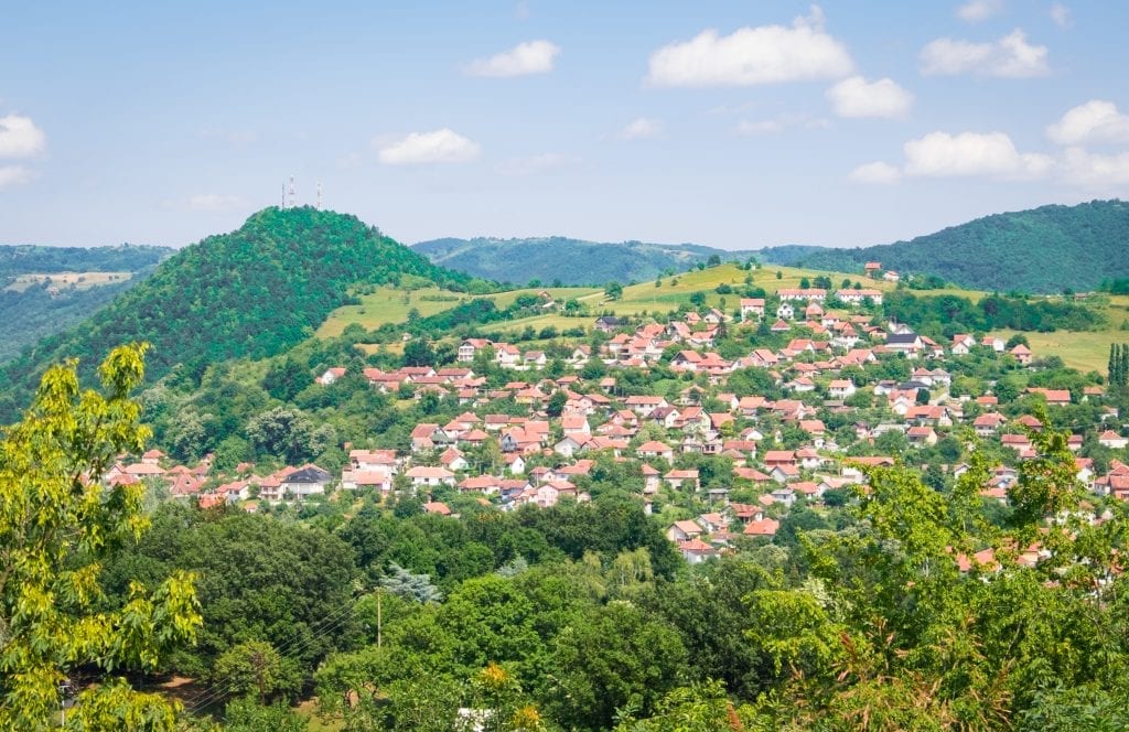 A hilly wooded area with lots of white cottages with terra cotta roofs in the distance.