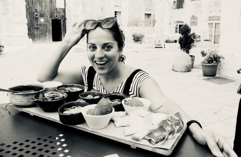 Kate crouches in front of a large spread of food, each in its own small plate, in Monopoli, Italy.
