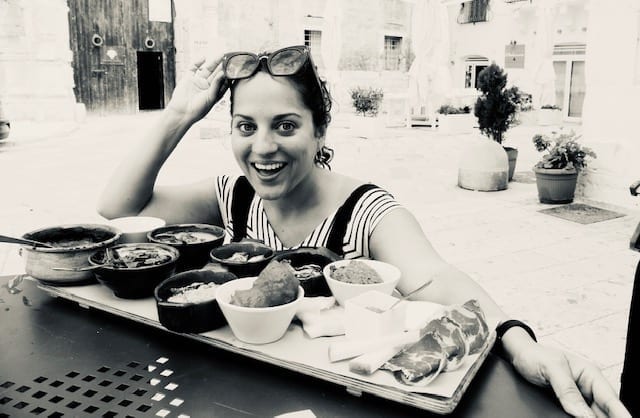 Kate crouches in front of a giant food platter filled with various small plates in Monopoli, Italy.