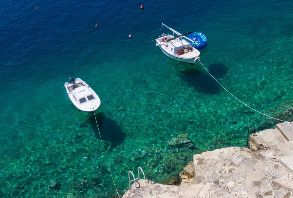 Two small white boats anchored in bright teal water leading to a rocky shoreline.