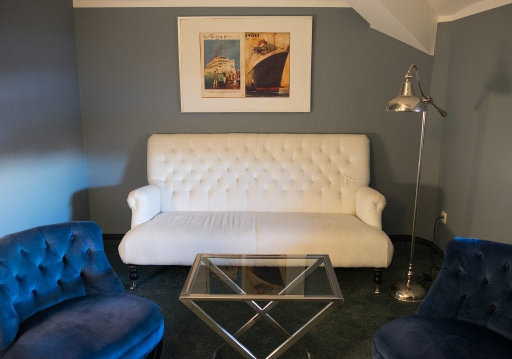 A white loveseat and framed photo of steamships above it; two navy blue chairs on each side.
