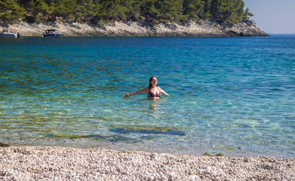 Kate swimming in the clear blue-green water at Pupnatska Luka, holding her arms outward and smiling, looking at the sky (actually I was just trying to make sure the light hit my face right).