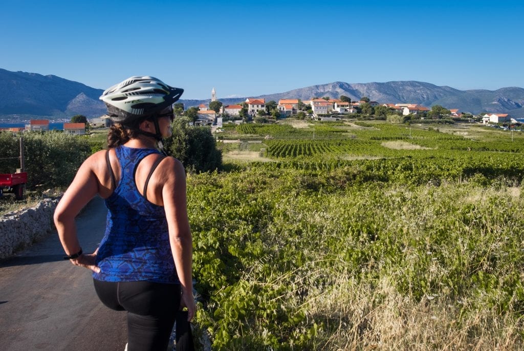 Kate wears a racerback top and bike helmet and stands with her hand on her hip, overlooking the vineyards of Lumbarda, Croatia.