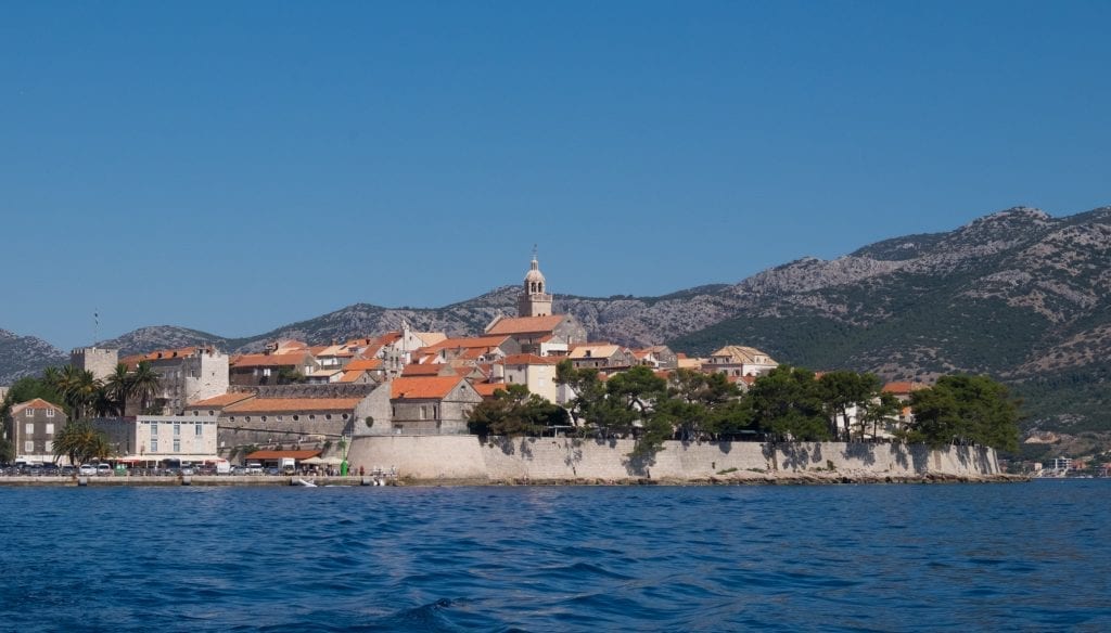 Korcula's walled old city rising up from the water, the mountains in the background.