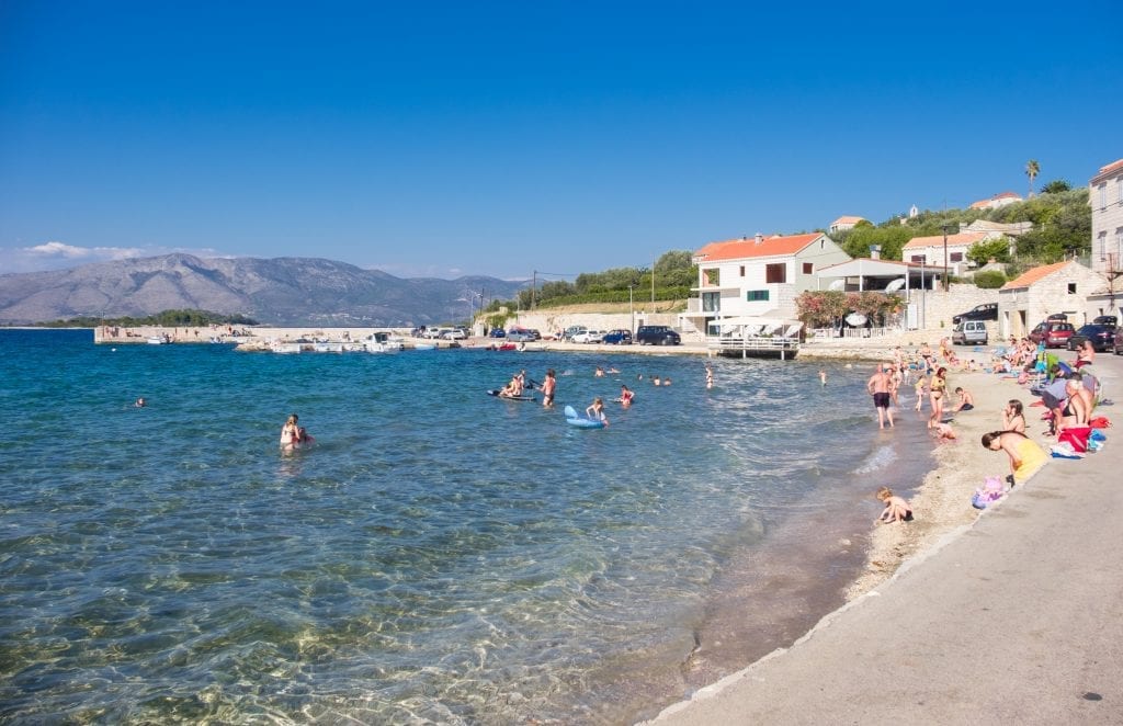 Families lounging on a sandy beach in Croatia, white stone buildings in the background.