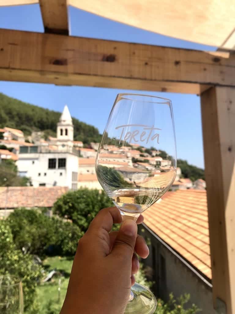 A glass of wine reading "Toreta" in the foreground; in the background, the small town of Smokvica with its church tower.