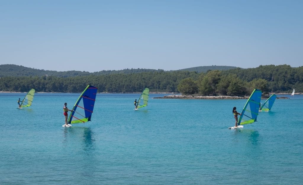 Several windsurfers practicing holding their sails up in the calm water near Badija Island.
