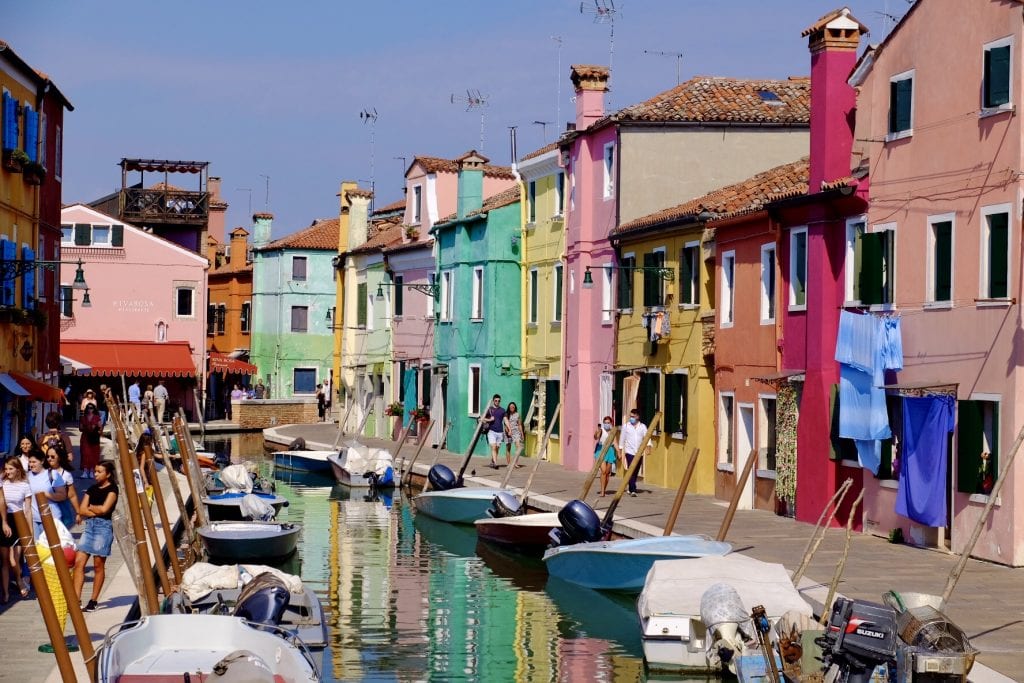 The brightly colored buildings of Burano island in Venice, all set on a canal filled with small boats.
