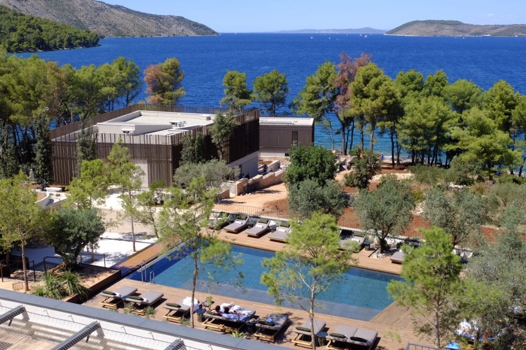 Maslina Resort: a view from above of a rectangular pool edged with seats, and a tree-edged shoreline and bright blue water.