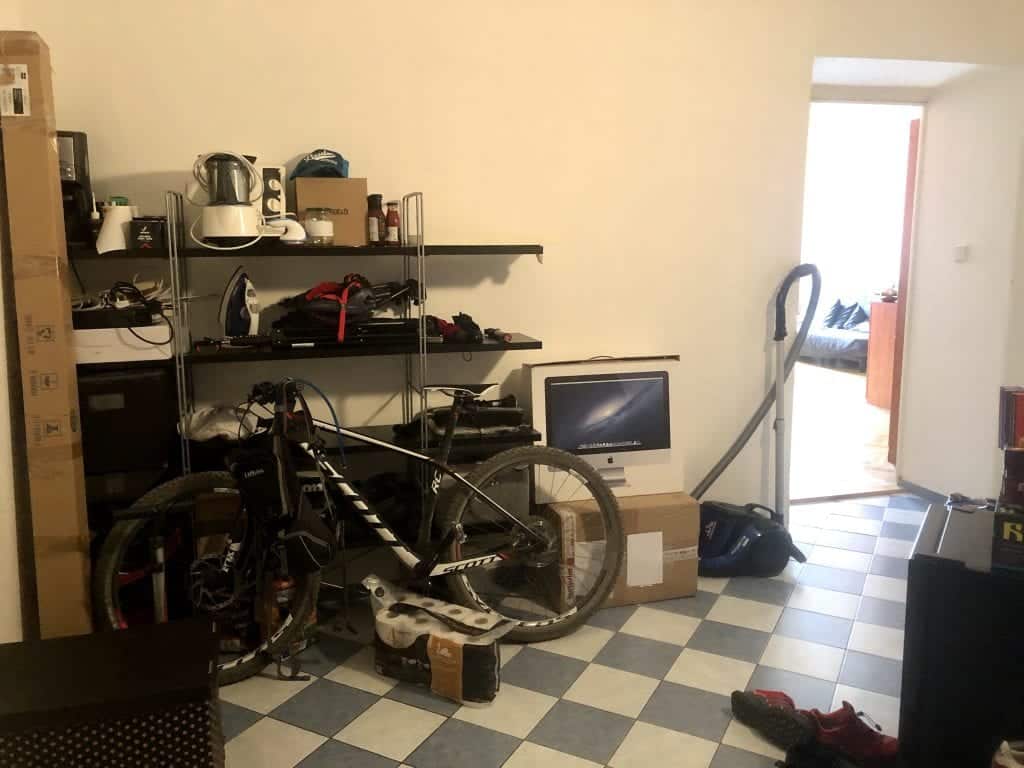 An entryway with cluttered open shelving and a bike and vacuum out in the open.
