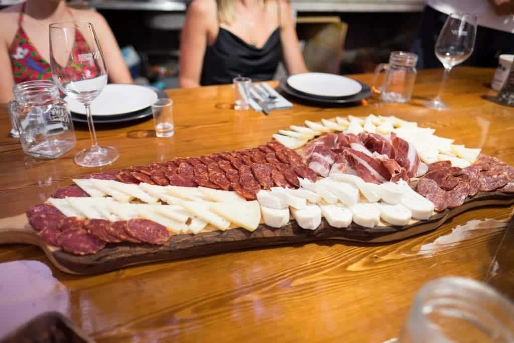 A long wooden tray covered with cured meats and sliced cheeses.