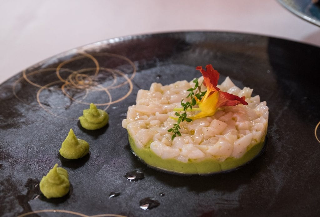 Scallop tartare with avocado arranged on a black plate with an orange flower on top