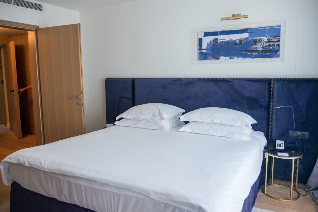 Bed in a room at Hotel Excelsior with white linens and pillows and a navy blue headboard