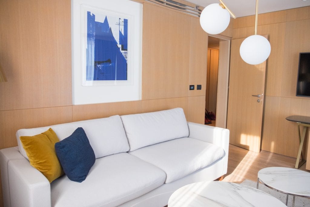 White couch with a blue pillow and yellow pillow on it, and a white and blue painting above it