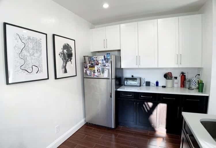 Kate's kitchen: white cabinets on top, black cabinets on the bottom, silver fridge topped with magnets, and black and white prints on the walls.