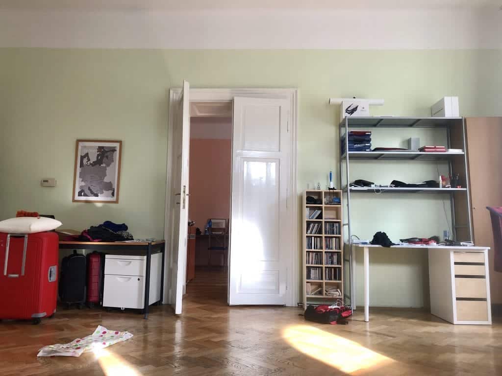 The glossy white doors from the indoor angle. On the left, a desk and lots of suitcases. On the right, a desk with lots of shelving, and a CD tower filled with CDs.