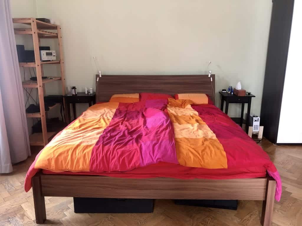 A close-up view of the bed with the pink, red, and orange bedspread. Two black nightstands on each side of the table.