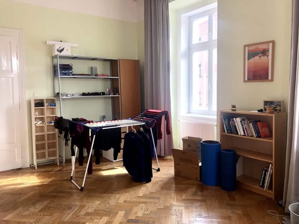 That same shelving unit with a drying rack with clothes hanging off it. A big window and a small bookshelf.