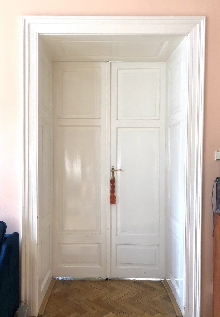Glossy tall white wooden doors that have a small square entryway of their own. An orange poofed lanyard hangs on the door handle.