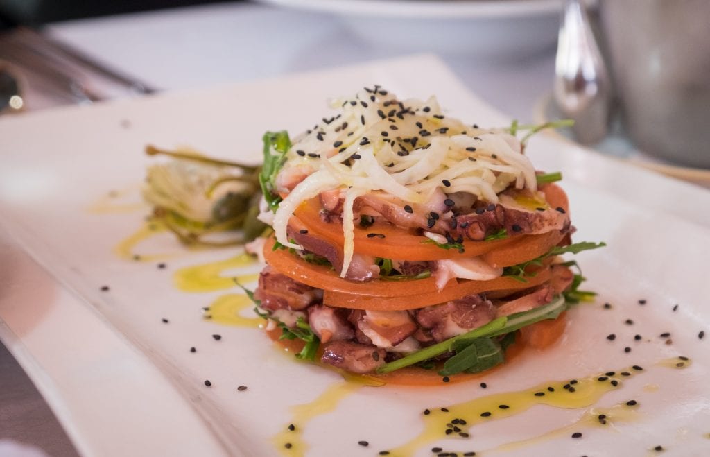 Octopus tartare stacked up colorfully on a white plate with poppy seeds on top