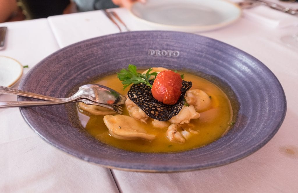 Ravioli with butter-poached shrimp in a blue bowl with a black crisp and tomato on top