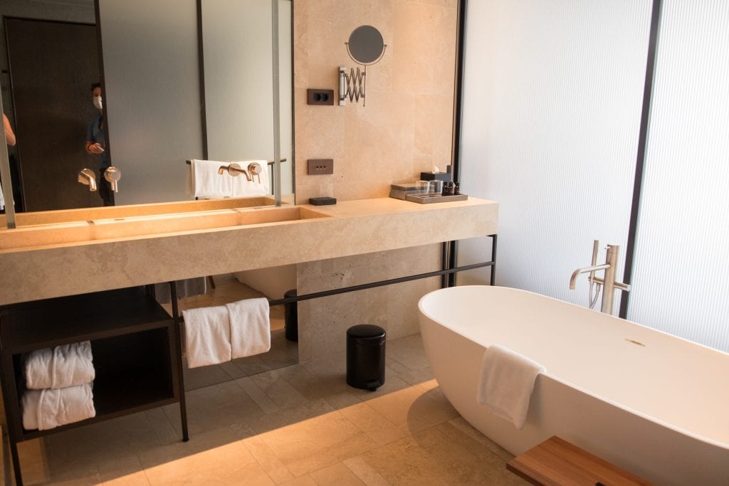 A beige-colored bathroom with a double sink and large bathtub.