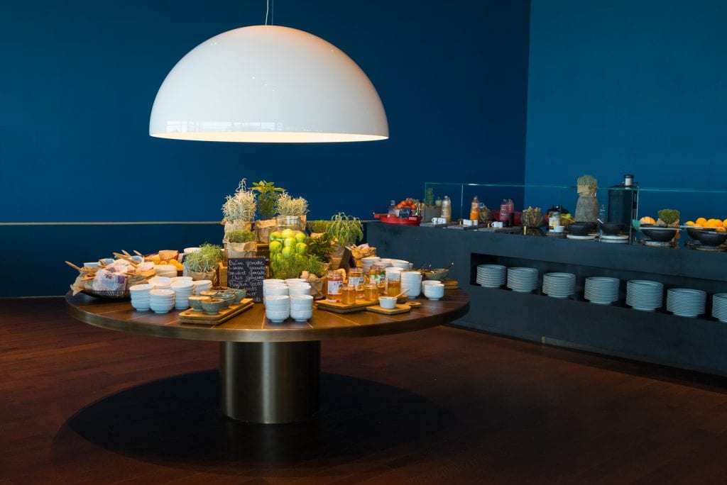 A golden buffet table in a dark blue room laid out with bowls, jams, and fruits.