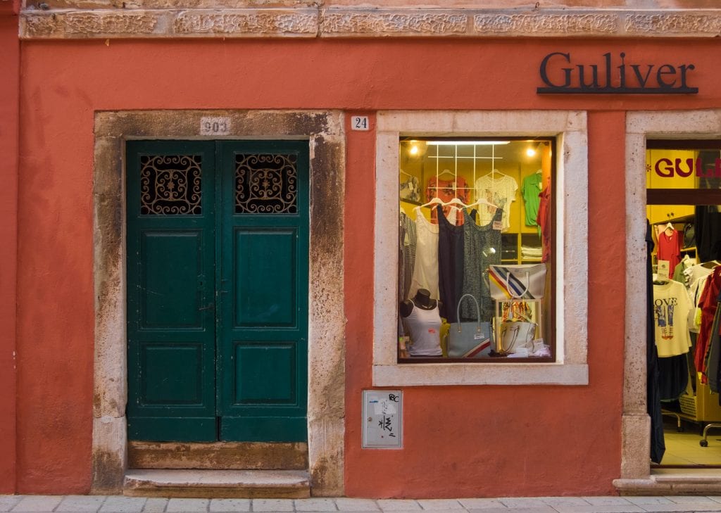 An ornate green door in the middle of a red-orange building next door to a boutique named Guliver.