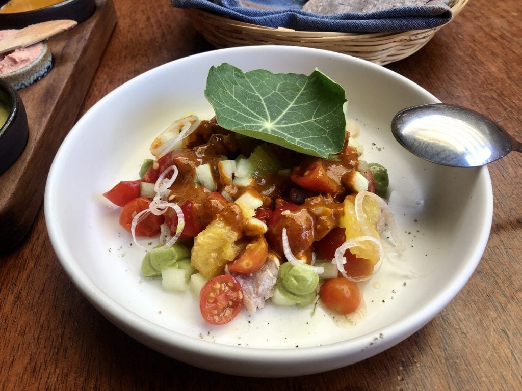 A fancy plate topped with ceviche, including fish, rounds of oranges, onions, and cherry tomatoes.