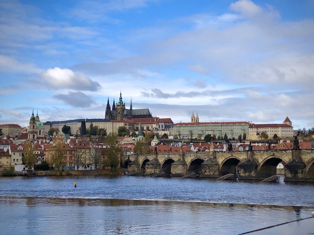 Prague Castle and St. Vitus's cathedral atop a hill; in the foreground, churches and the Charles Bridge, all set on the river.