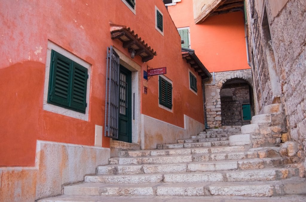 A stone staircase leading upward in Rovinj, surrounding walls are a deep earthy red shade.