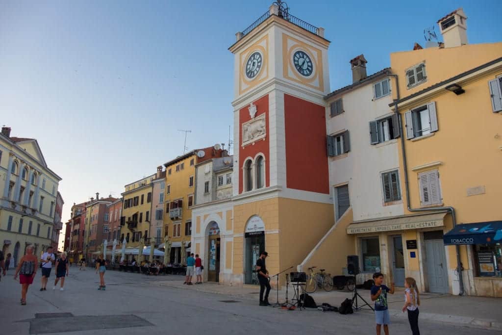 The white, red, and yellow clock tower in Rovinj, two kids talking in the foreground.