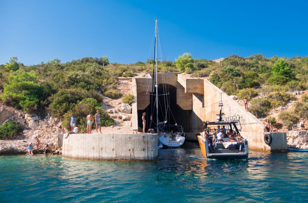 A submarine tunnel coming out of a hill in Vis, emerging into the ocean. Sailboats are sailing into the tunnel and people hang out on either sides of the tunnel.