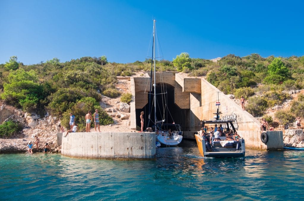 A submarine tunnel coming out of a hill in Vis, emerging into the ocean. Sailboats are sailing into the tunnel and people hang out on either sides of the tunnel.