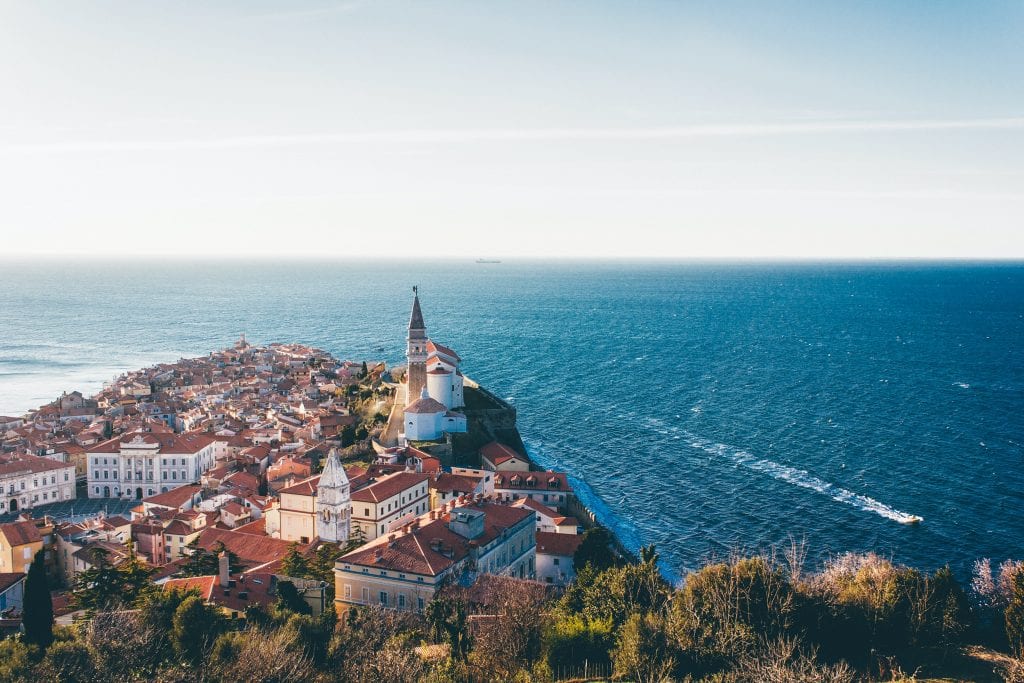 Piran, Slovenia: a town with white buildings and red roofs on the edge of the ocean.