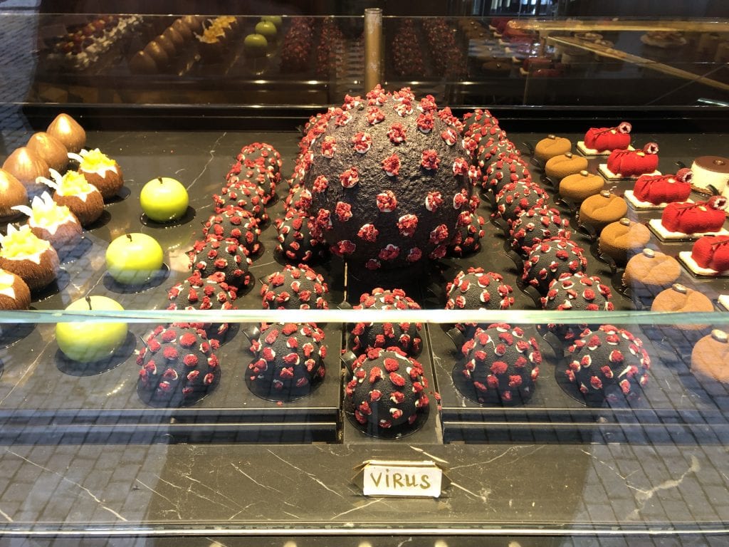 A bakery window with dark brown round cakes with red and white frosting dots to look like the coronavirus. A label in front reads VIRUS.
