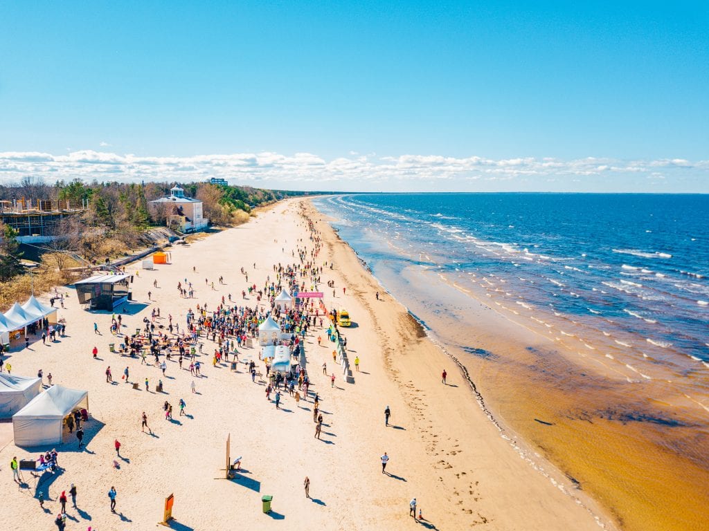 A long, wide beach covered with people and small white tents. The ocean is blue with lots of waves. Nobody is swimming, LOL.