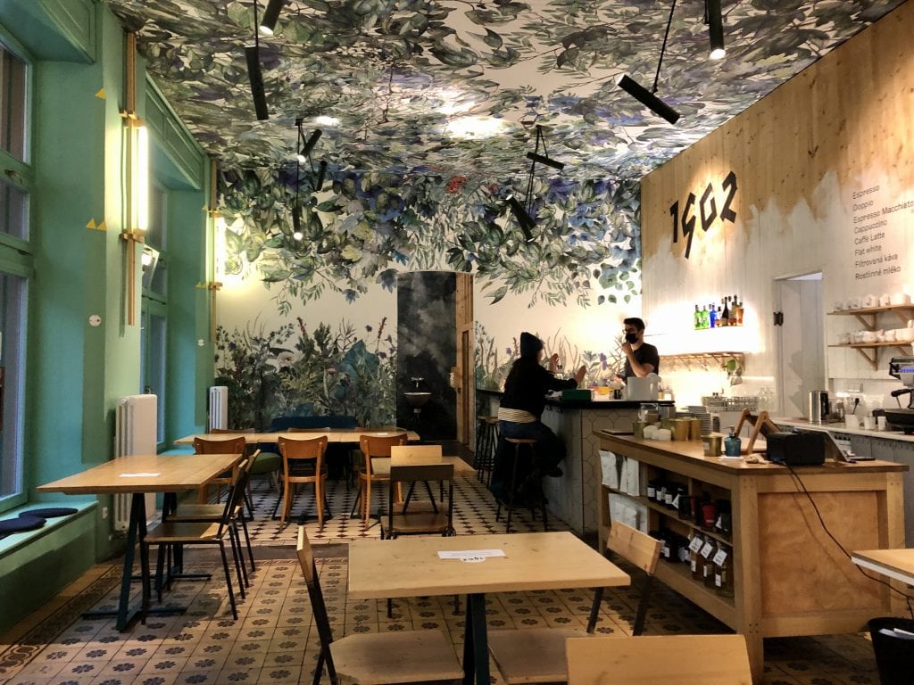 A chic Prague cafe with painted green leaves decorating the ceiling.