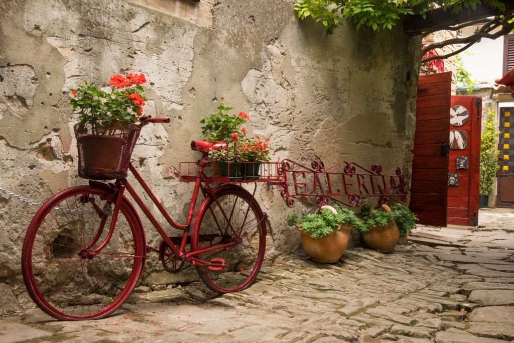 A red decorative bicycle with red geraniums in its basket in Grožnjan, Croatia.